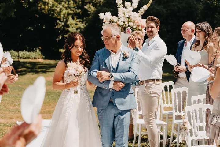 De bruid loopt aan de arm van haar vader naar de ceremonie